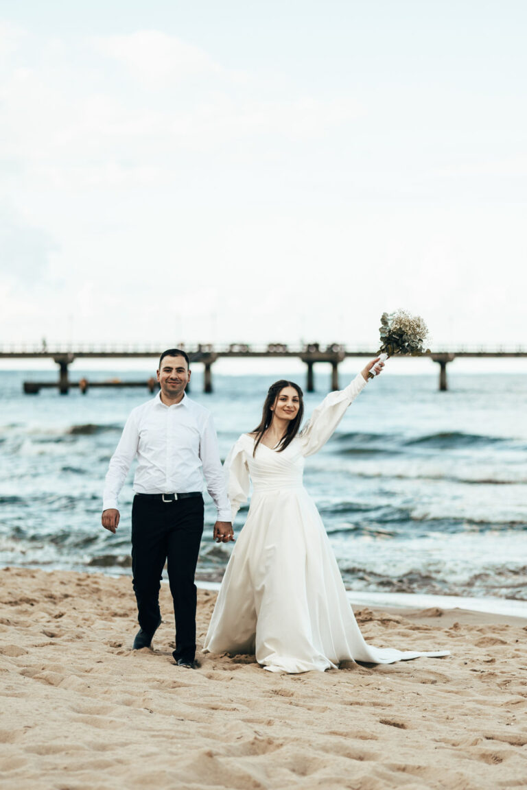 Jaqui.Fotografie / Brautpaar geht am Strand entlang.